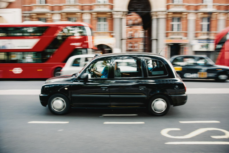 Capturing a black taxi speeding through the streets of London with iconic red buses in the backdrop.