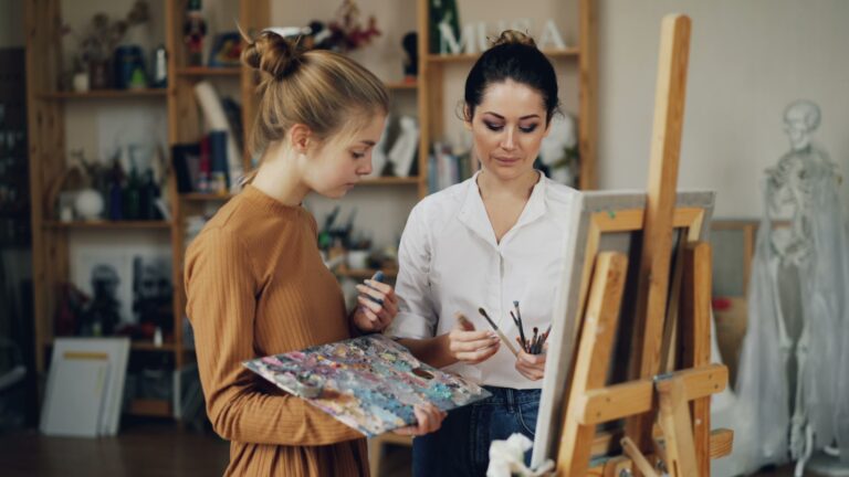 Two women paint at an easel together.