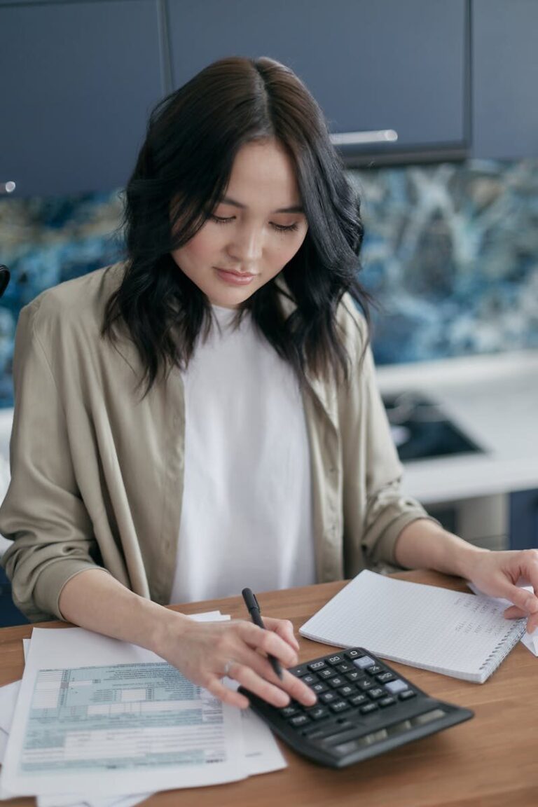 Woman using a calculator for budgeting and finance management at home desk.